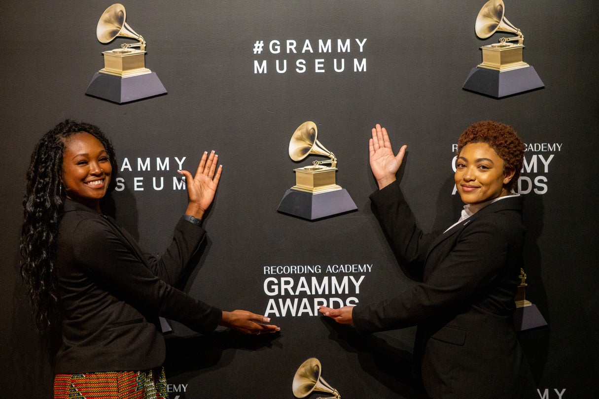 Two women posing in front of the Grammy Awards step and repeat backdrop