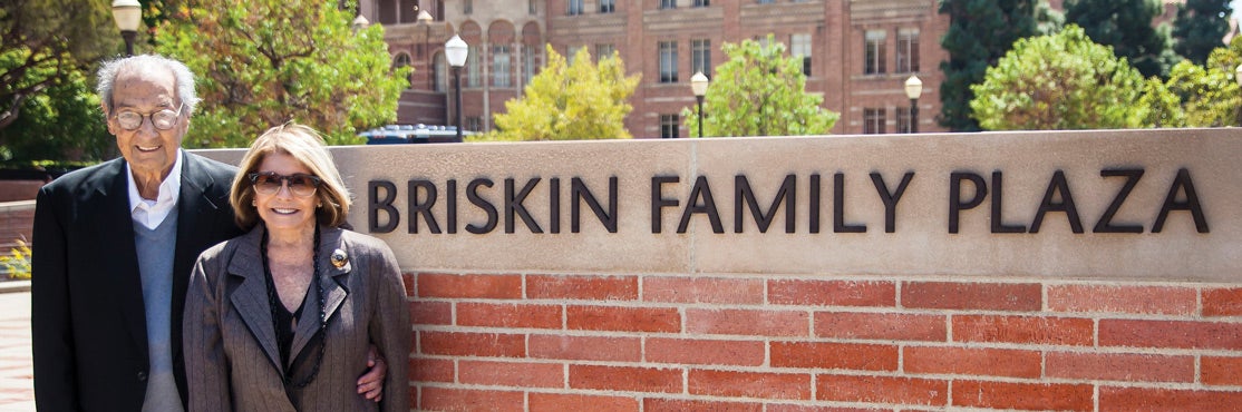 Bernard Briskin with partner standing next to Briskin Family Plaza sign