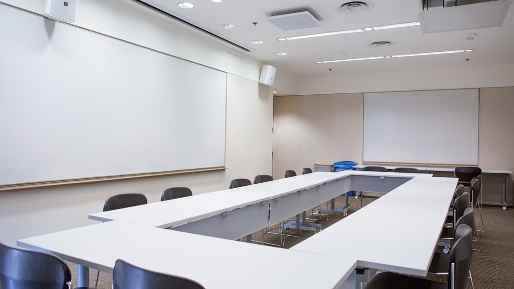 Empty flat classroom space at UCLA Anderson with tables arranged in a rectacle and two whiteboards mounted on wall