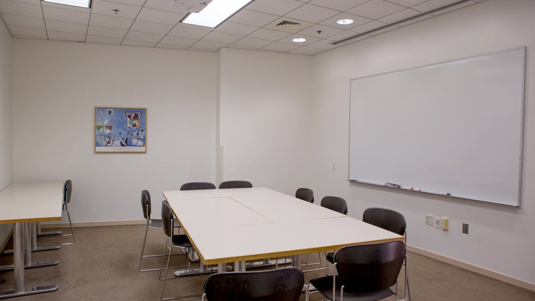 Empty seminar room 2 at UCLA Anderson with square tables, movable chairs and mounted whiteboard