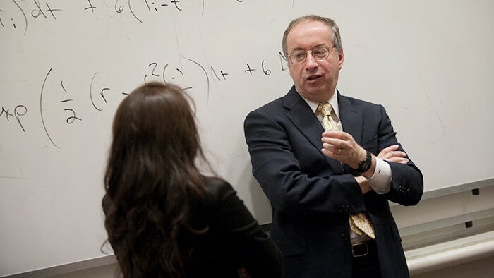 Professor in conversation with student in front of a whiteboard