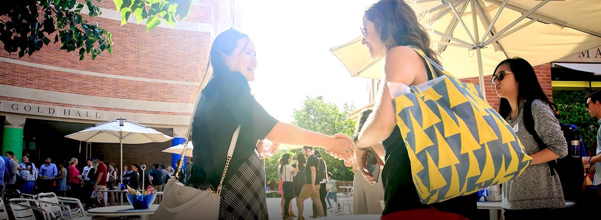 Two women shaking hands at the UCLA Anderson courtyard
